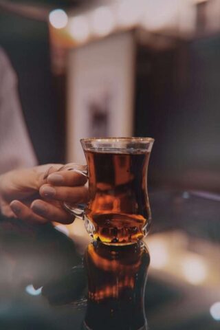 A cozy evening indoor setting with a glass of black tea being held by a delicate hand.