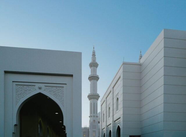 Photo by Cocodillaa.com A tall minaret rises between modern white buildings.