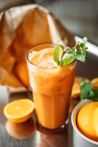 Photo by Cocodillaa.com Close-up of a refreshing orange juice with mint leaves, surrounded by fresh oranges.
