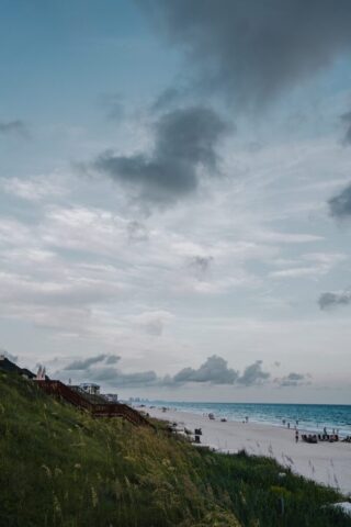 A beach with people walking on the sand and a cloudy sky