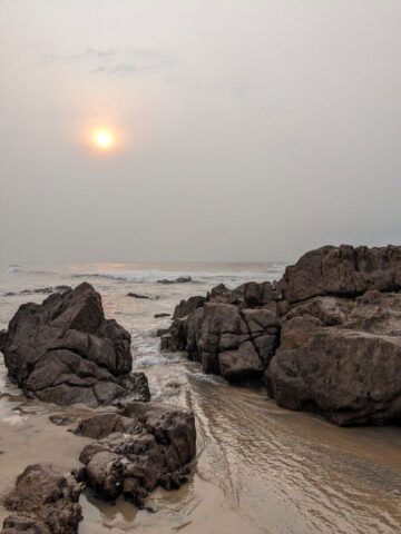 the sun is setting over a rocky beach