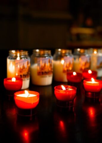 Photo by Cocodillaa.com Several lit red votive candles and jars in darkness.