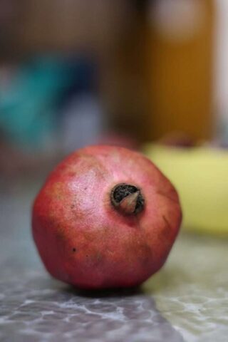 A single ripe pomegranate rests on a patterned surface.