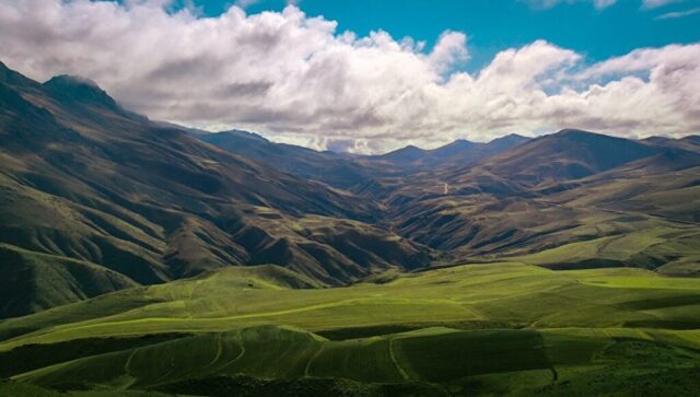Photo by Cocodillaa.com green grass field and mountains under white clouds and blue sky during daytime