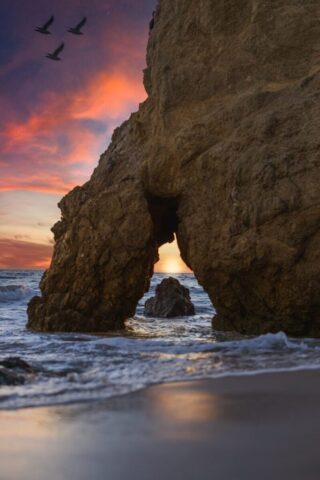 a rock arch with birds flying around