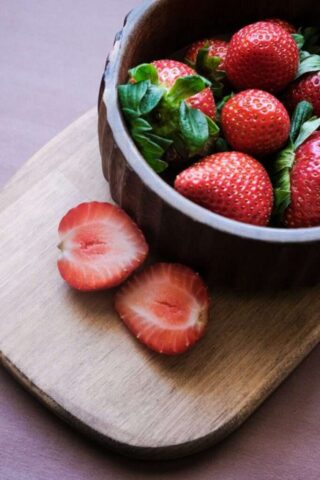 a bowl of strawberries on a cutting board