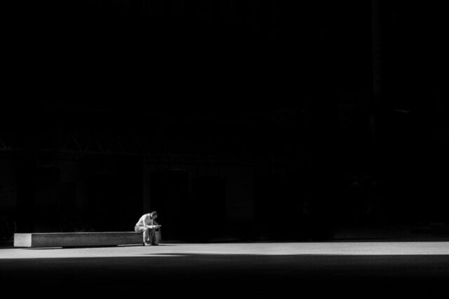 grayscale photogaphy of man sitting on concrete bench
