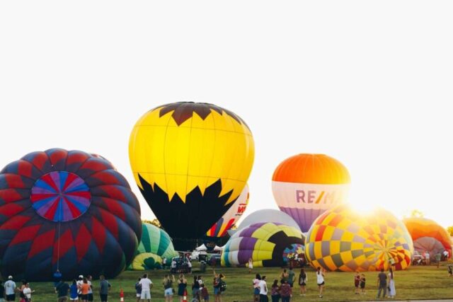 Photo by Cocodillaa.com A group of people standing around a bunch of hot air balloons