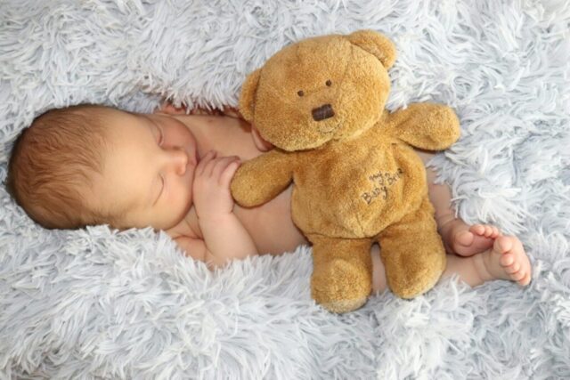 Photo by Cocodillaa.com baby lying on white fur textile beside brown bear plush toy