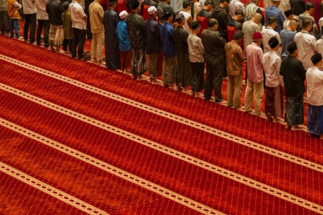 Photo by Cocodillaa.com A group of men stand in prayer on a red carpet.