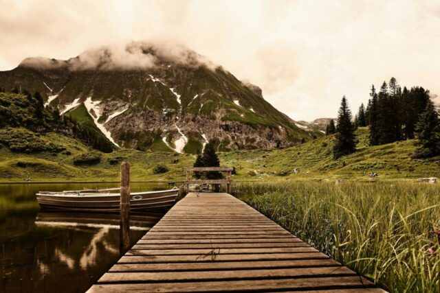 Photo by Cocodillaa.com brown wooden dock on green grass field near mountain during daytime