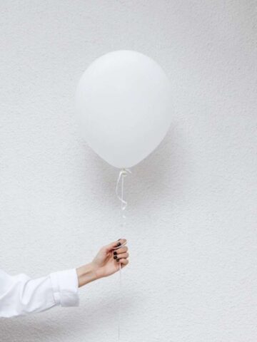 Photo by Cocodillaa.com person holding white balloons near white wall