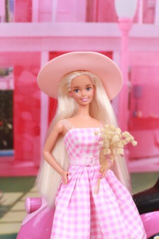 A barbie doll in a pink dress and hat on a pink motorcycle