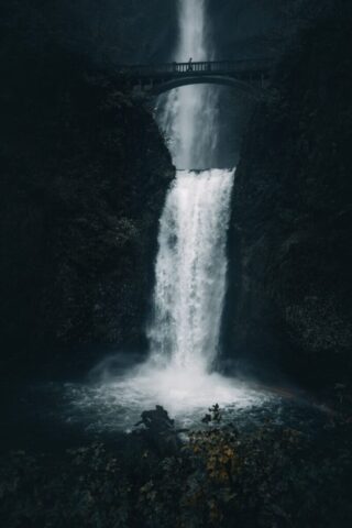 Majestic waterfall cascades down a rocky cliff with bridge.