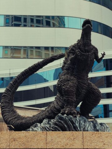Photo by cocodillaa.com A godzilla statue stands in front of a modern building.