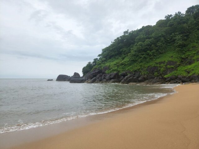 A sandy beach next to a lush green hillside