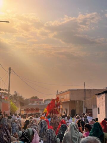 A parade passes through a crowded street at sunset.