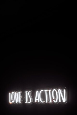 Minimalist neon sign with 'Love is Action' on a dark background.