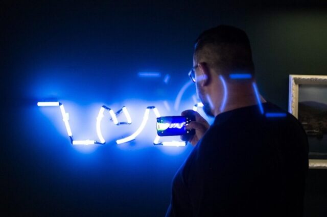 neon sign, man, mobile phone, phone camera, smartphone, taking picture, person, neon, neon blue, lights, glow, illuminated, signage, dark
