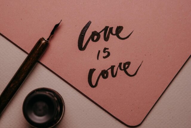 Close-up of 'love is love' written in elegant calligraphy with a fountain pen and ink bottle.