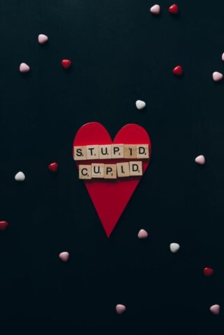 Heart-shaped card with 'Stupid Cupid' spelled out on scrabble tiles, surrounded by small hearts.