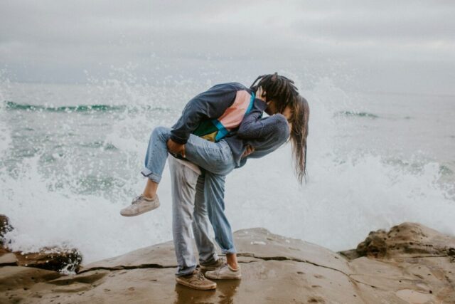 Photo by Cocodillaa.com woman in blue jacket and gray pants carrying woman in blue jacket on beach during daytime