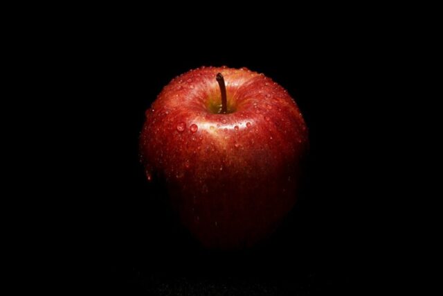 a red apple sitting on top of a black table