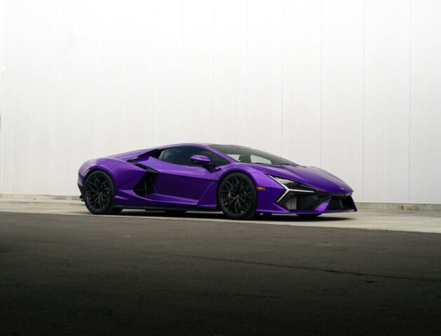 A sleek purple sports car parked against a white wall.
