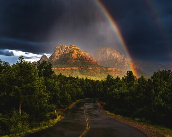 Photo by Cocodillaa.com A rainbow appears over a road with a mountain in the background
