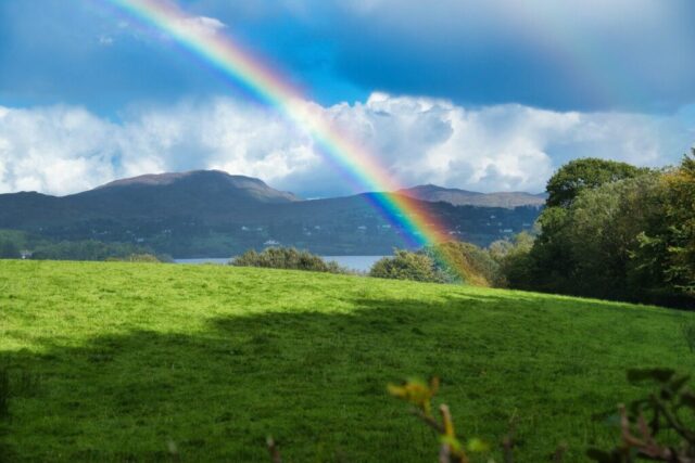 Photo by Cocodillaa.com a rainbow in the sky over a lush green field