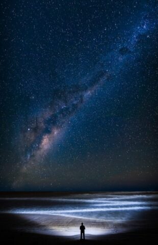Photo by Trevor McKinnon a man standing on top of a beach under a night sky